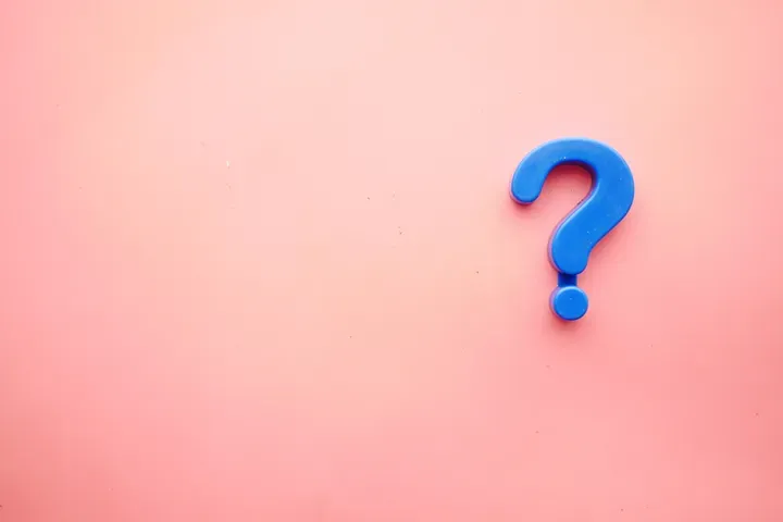 A blue question mark magnet on a pink background.