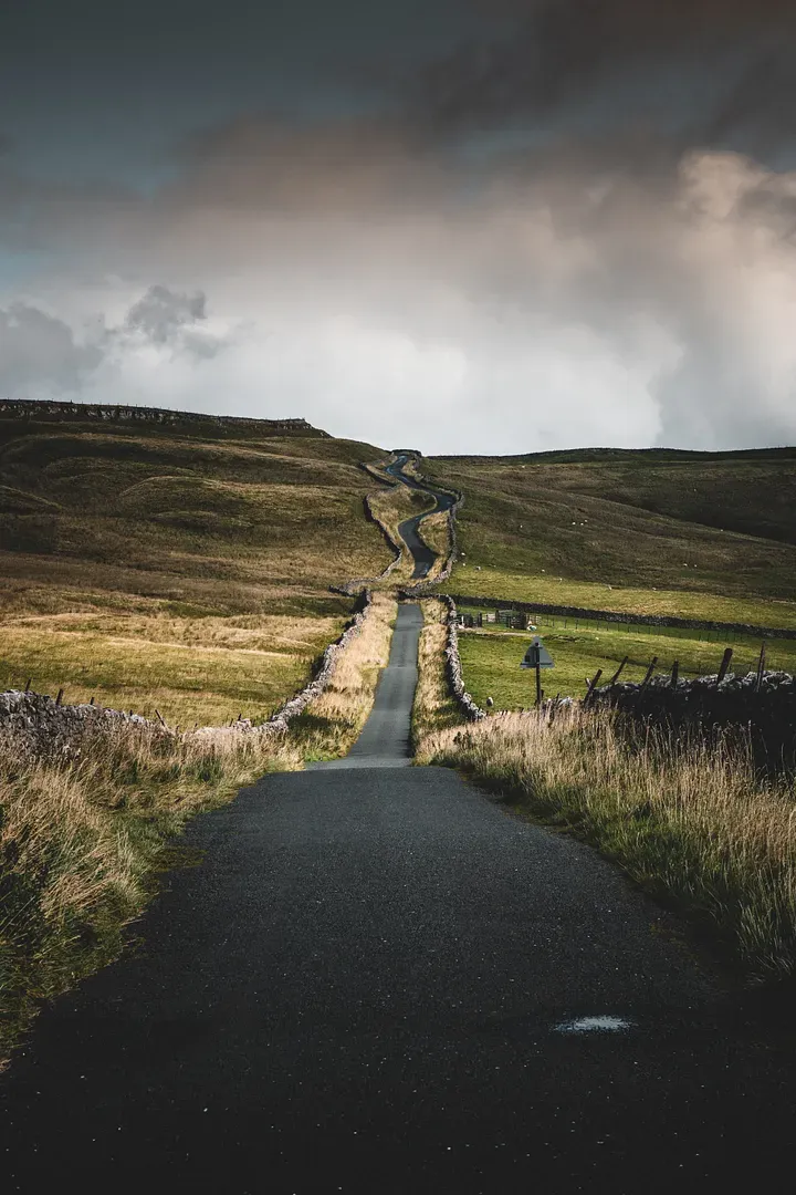 A view looking down a long paved road in the hilly countrysiide