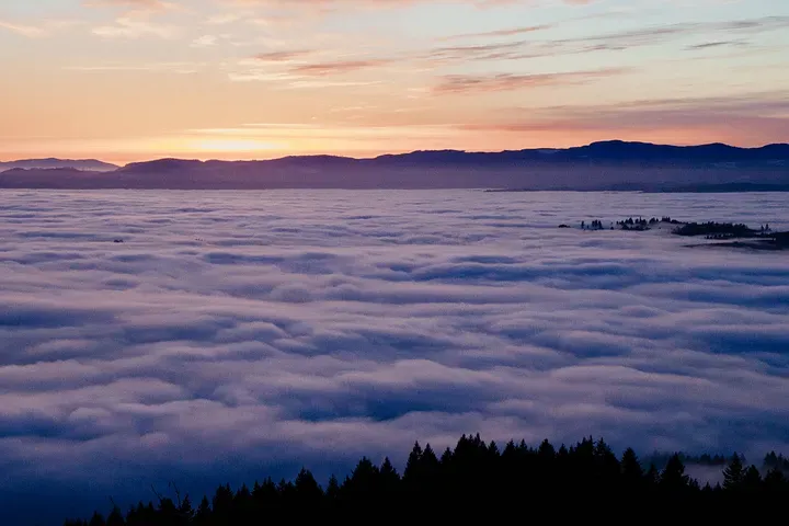 A view of a mountainous forest above the clouds as the sun sets.