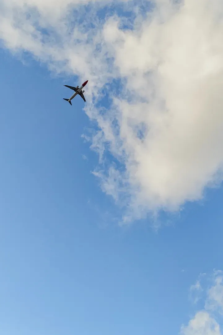 A blue sky with a few clouds and a plane flying overhead.