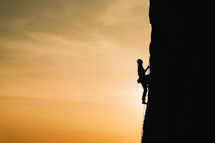 A silhouette of a woman climbing a cliff face. 