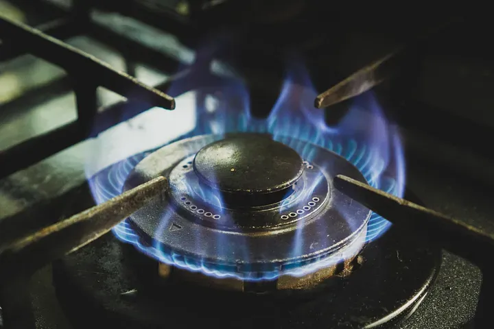 A closeup of a blue flame on a gas stovetop burner.