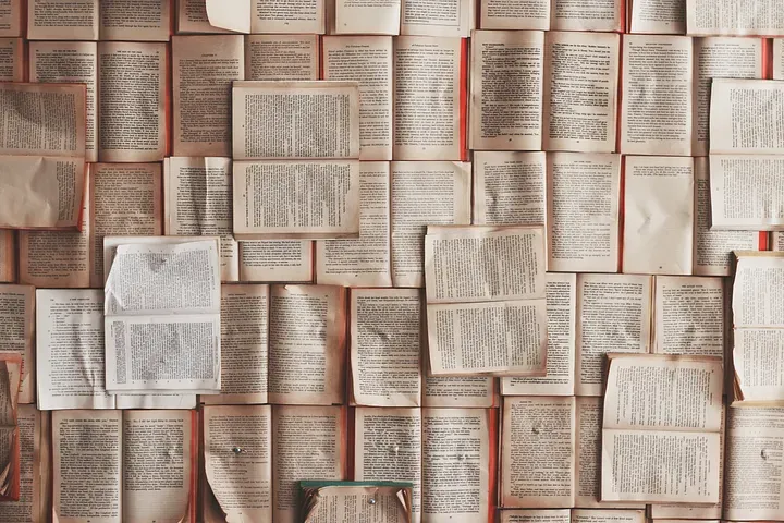 An assortment of tiled books, open with the spine laying flat displaying the text on their pages.