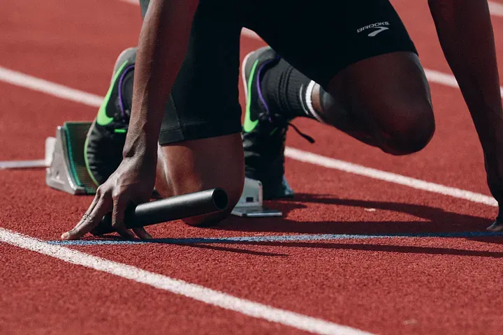 A closeup of a runner's feet on the starting blocks. The runner is holding a baton.