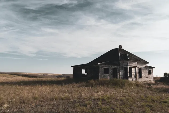 A small house on a field overlooking the rest of the land with an overcast sky above.